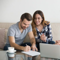Three coworkers discussing documents beside a laptop on a couch, with coffee cups nearby.