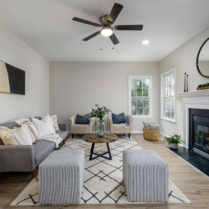 Bright living room with gray sofa, striped ottomans, fireplace, round mirror, and ceiling fan