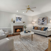 Bright living room with fireplace, gray sofas, white decor, and a ceiling fan