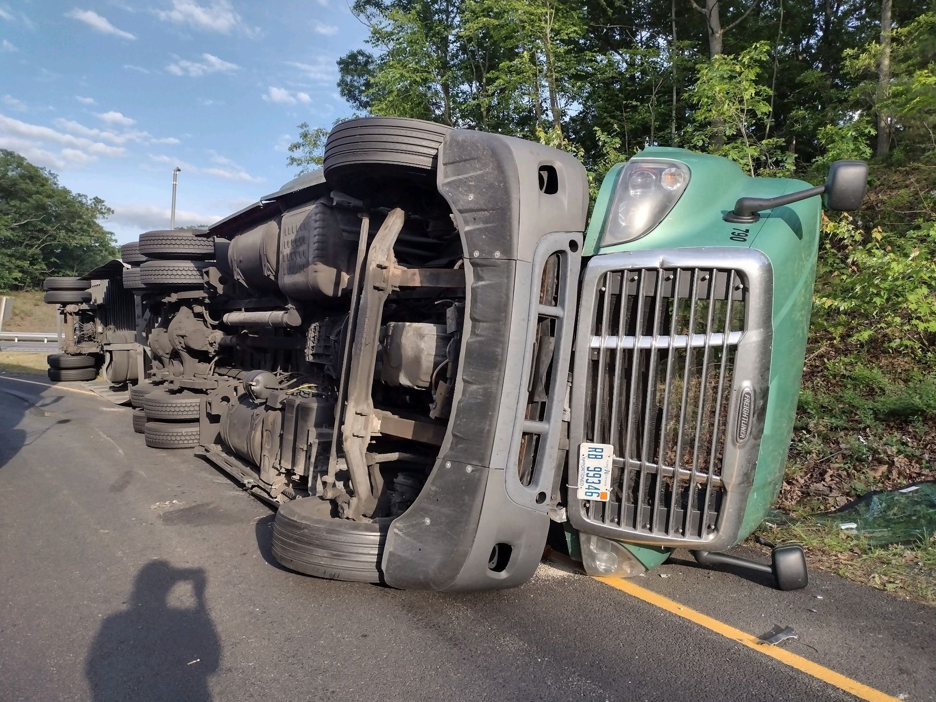 Green semi-truck overturned on a road, blocking a lane.