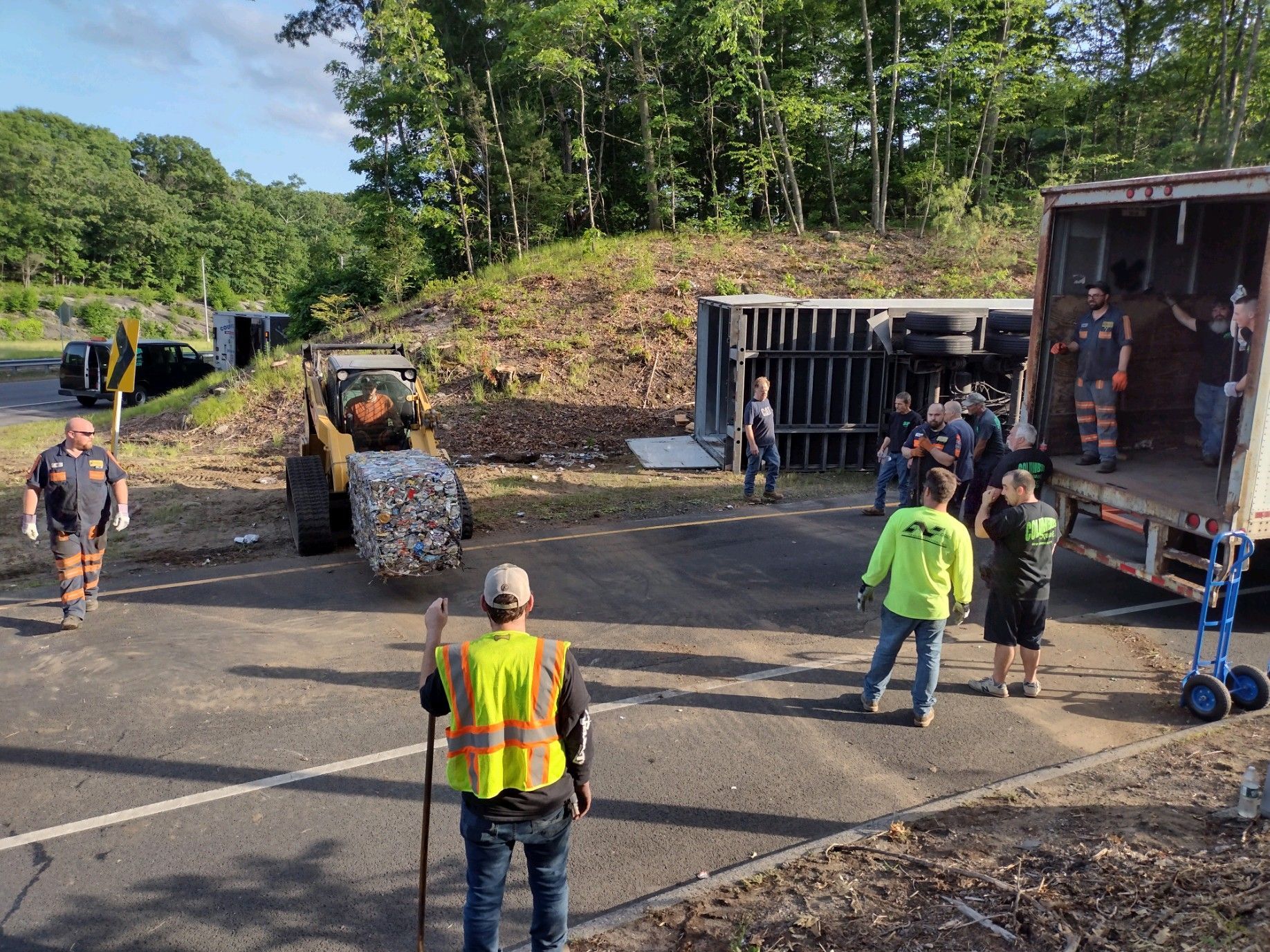 Workers and vehicles at a truck accident scene. A semi-truck is overturned.
