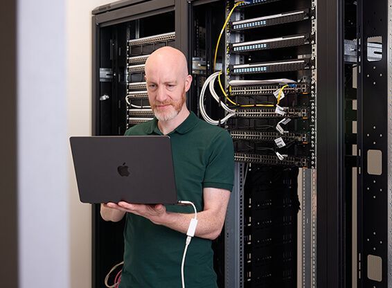 A man is using a laptop computer in a server room.