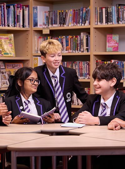 A group of children in school uniforms are sitting at a table in a library.