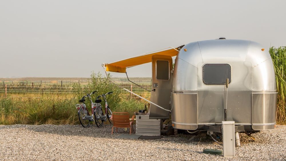 Silver Camper Trailer With Yellow Awning Beside Bicycles in a Rural Field — Edmonton Battery Centre in Edmonton, QLD