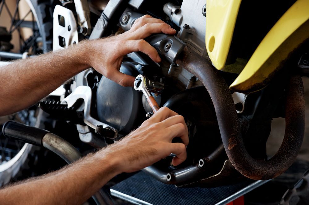 Hands Repairing a Motorcycle Engine With Tools, Showing a Yellow Bike Fairing — Edmonton Battery Centre in Mt Sheridan, QLD
