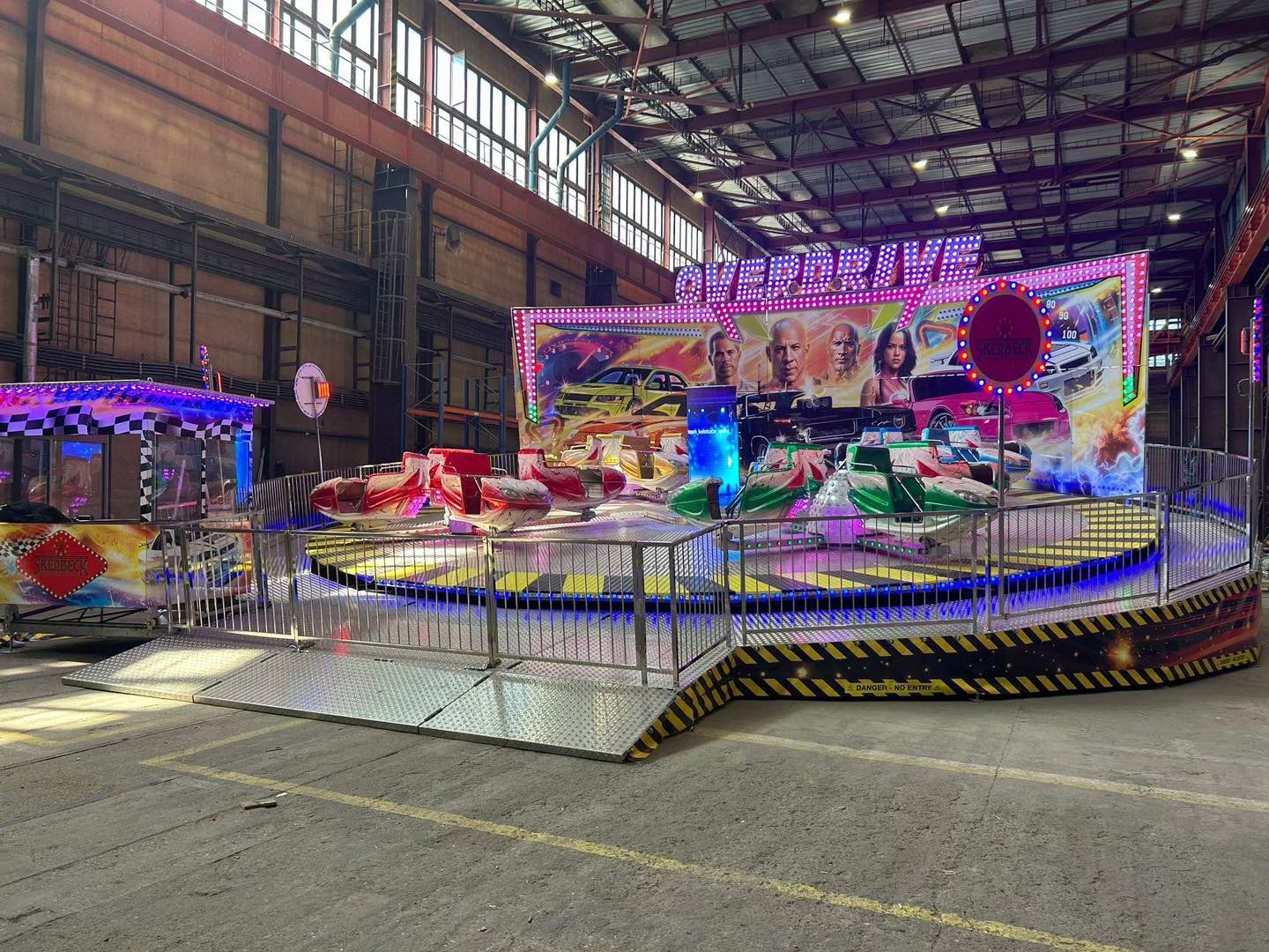 A colorful, circular carnival ride featuring movie-themed artwork, set within a large, industrial indoor space.