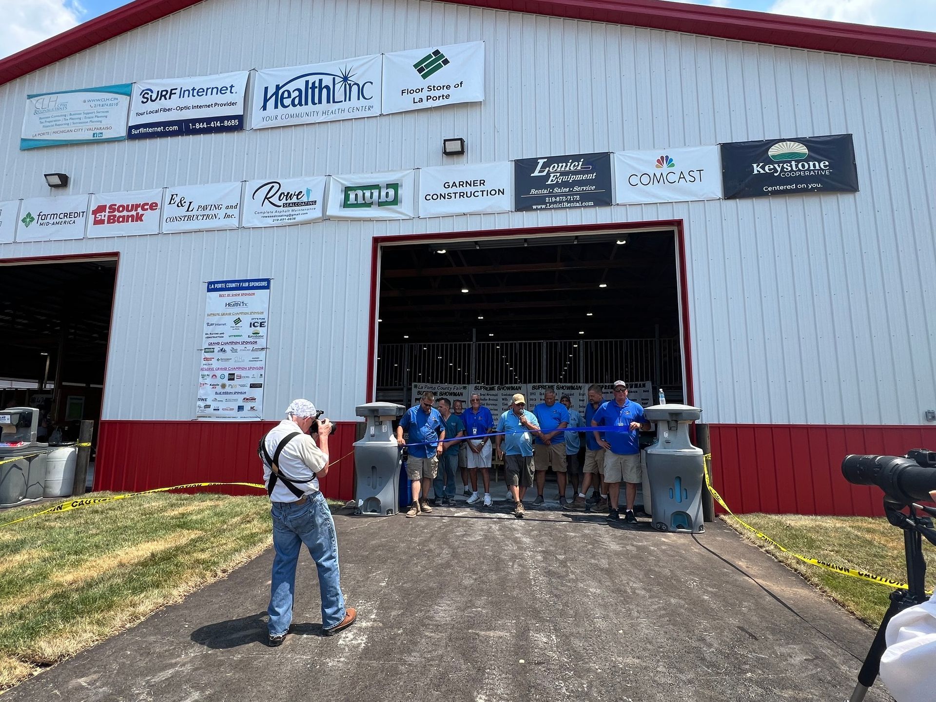 A group walks out of a building under many sponsor signs while a photographer captures the event.