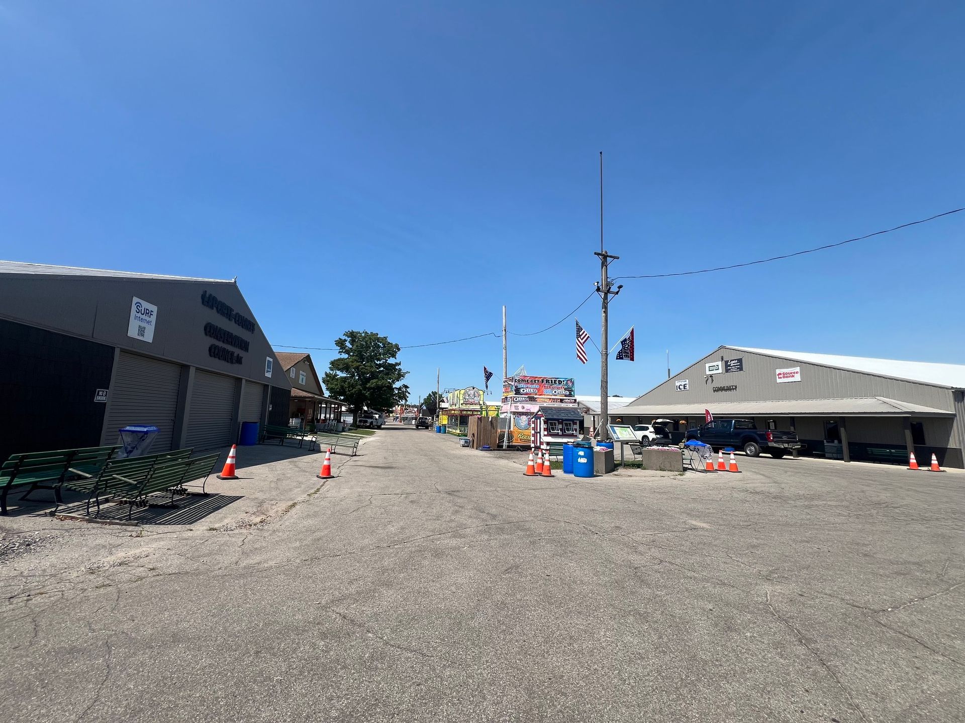 A gravel path between two large, grey metal buildings under a clear blue sky, with orange safety cones placed along sides.