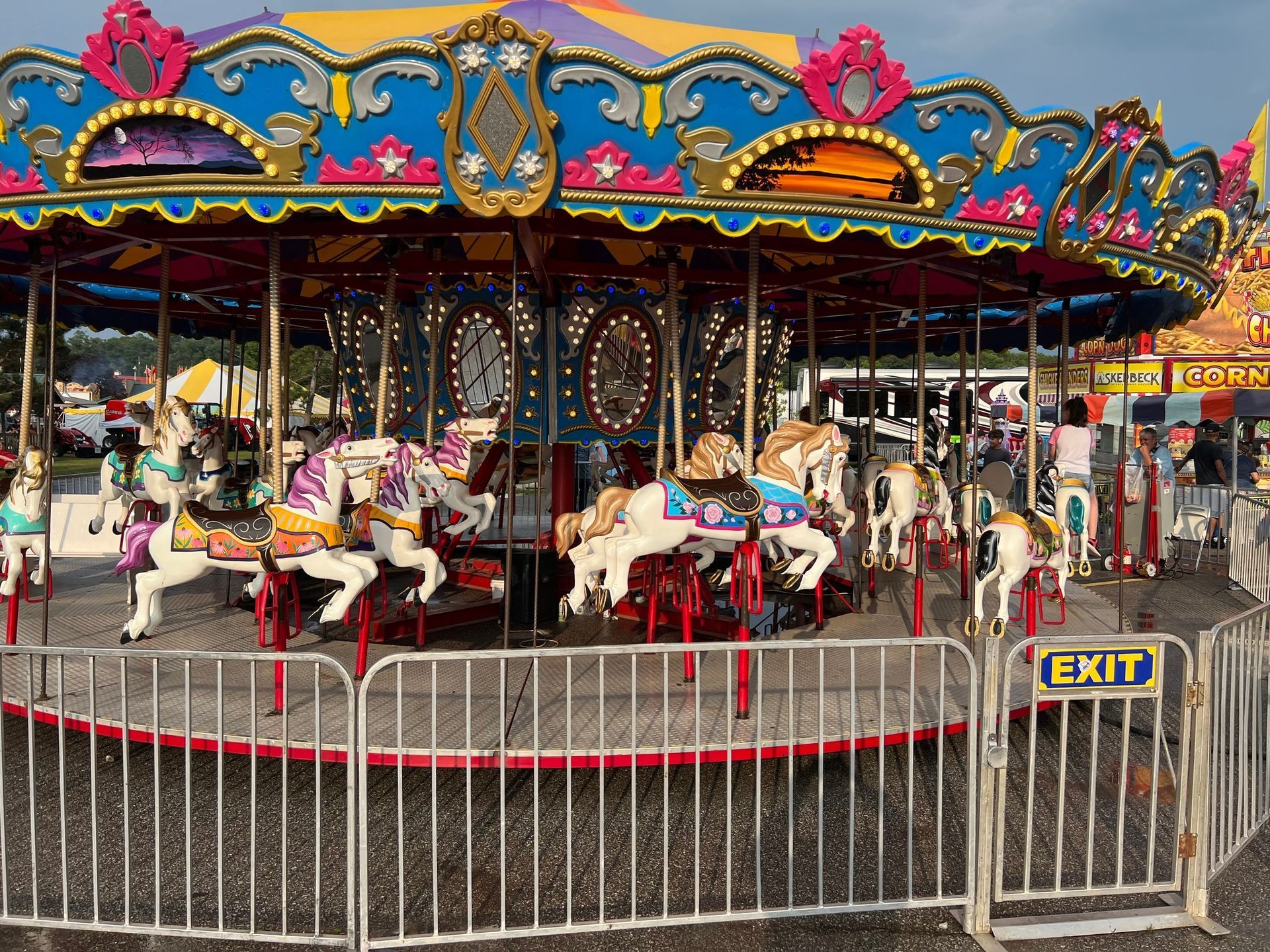 A colorful carousel at an outdoor fair, featuring several decorative horse ride-ons surrounded by a metal fence.