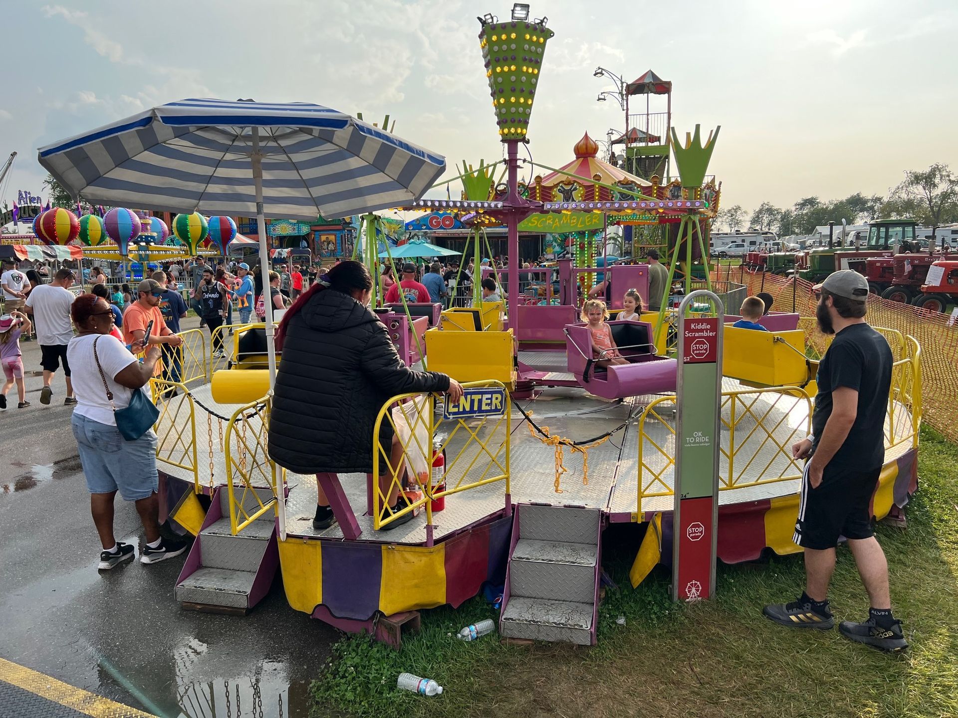 A colorful, spinning carnival ride at an outdoor fair with people standing around waiting for their turn.