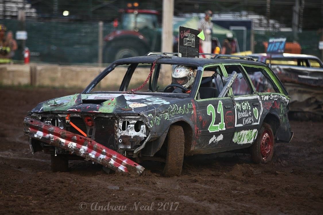 A black station wagon with the number 21 painted on the side participates in a dirt track demolition derby.