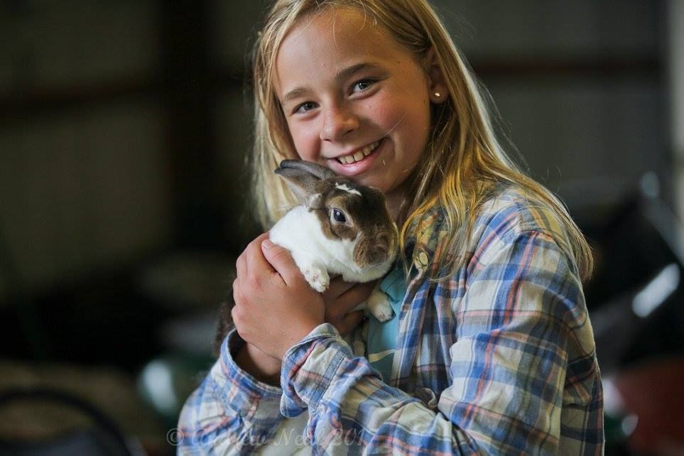 A smiling person wearing a plaid shirt holds a small brown and white rabbit in their arms.