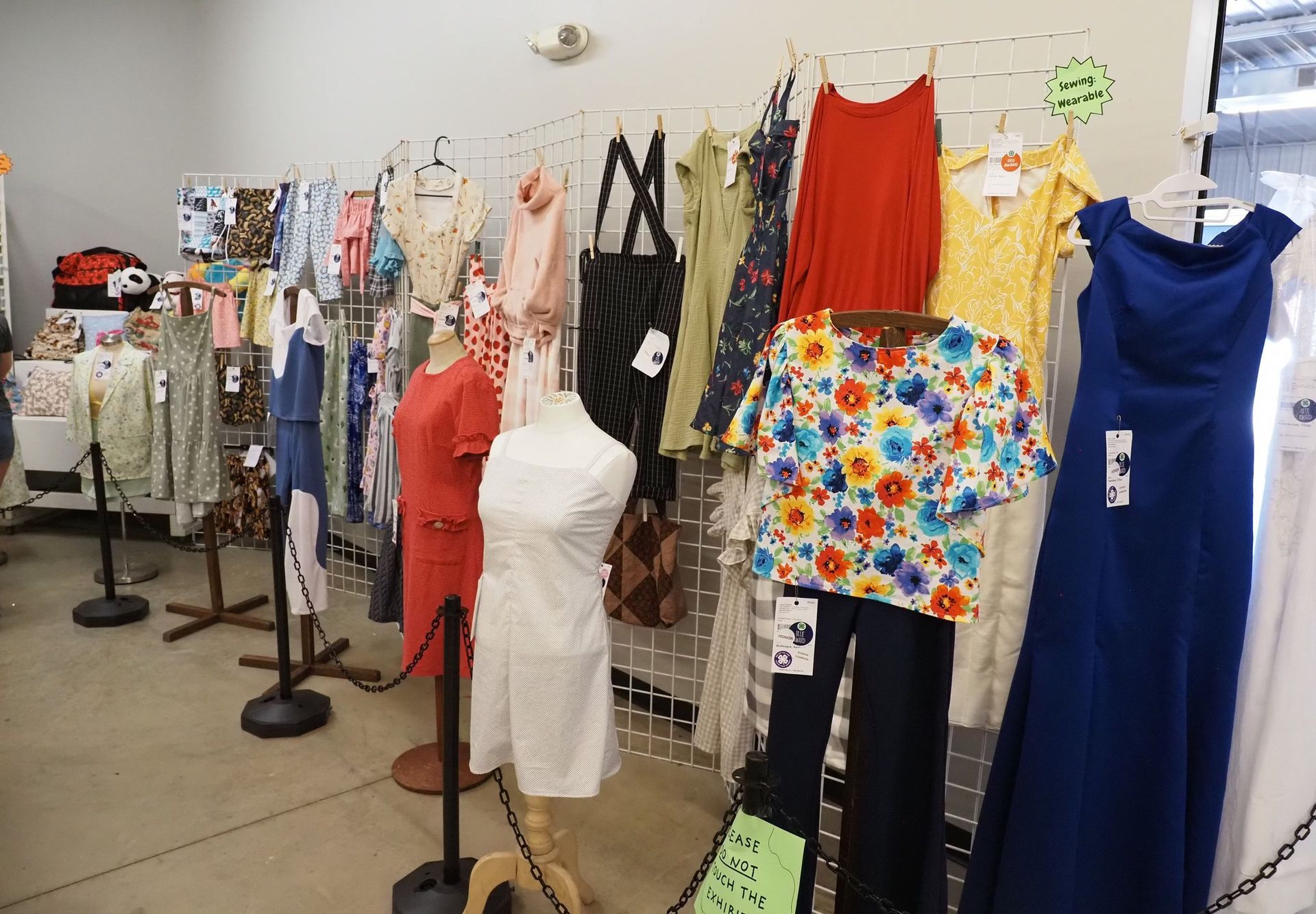 A clothing store display featuring various dresses, tops, and pants hanging on a wire rack and on mannequins.