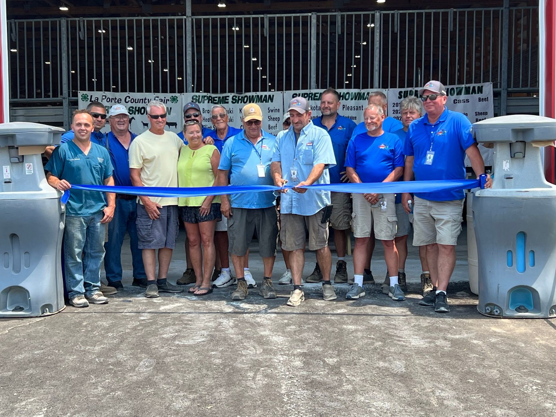A group of people standing together outdoors while holding a blue ribbon, likely at a ceremonial ribbon-cutting event.
