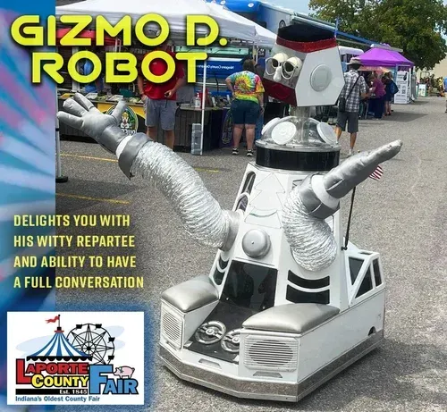 Gizmo D. Robot, a white-and-silver robot with flexible arms, stands at the LaPorte County Fair in a paved outdoor area.