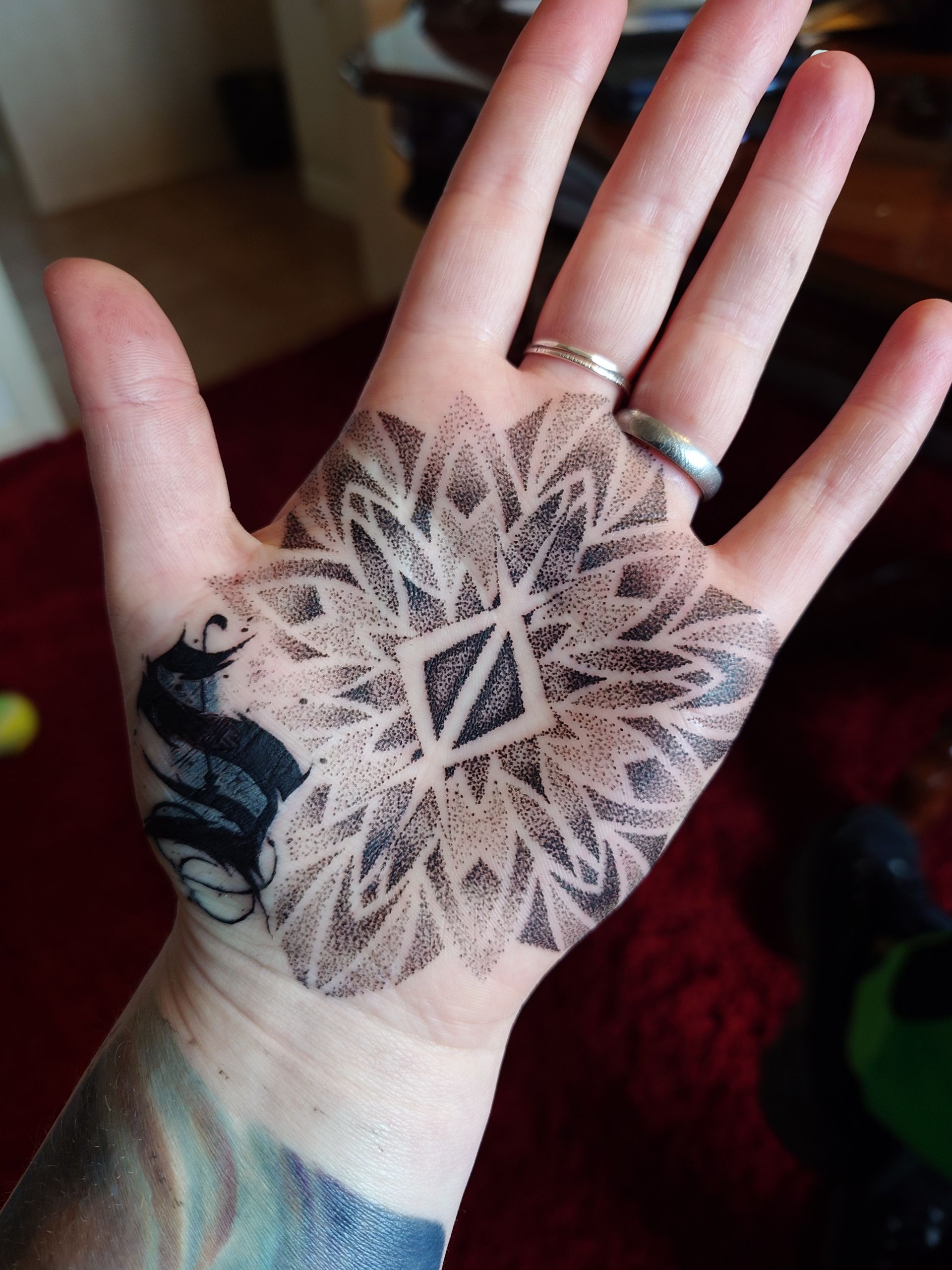 A person with a tattoo on their hand has a ring on their finger