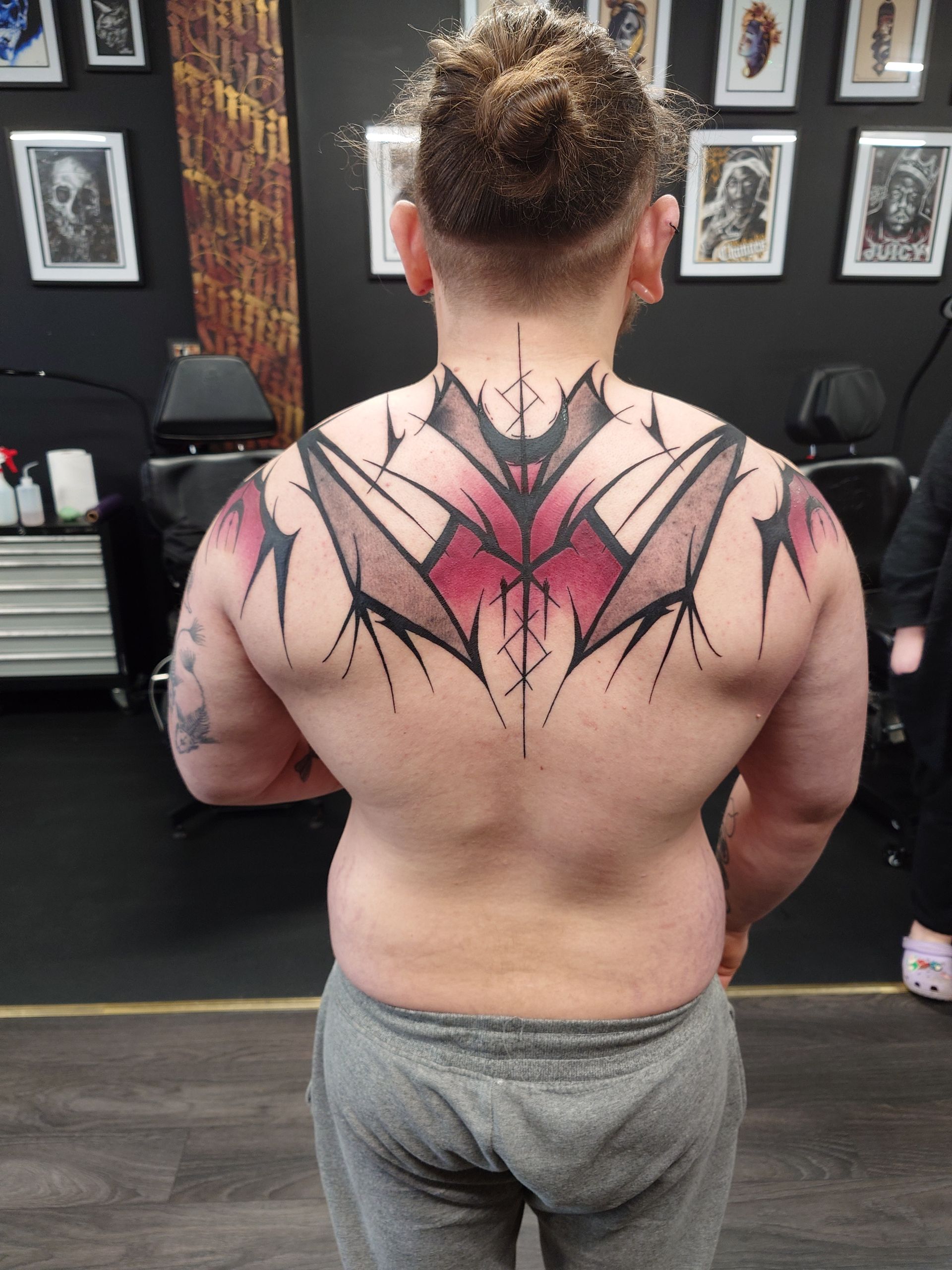 A man with a tattoo on his back is standing in a room.