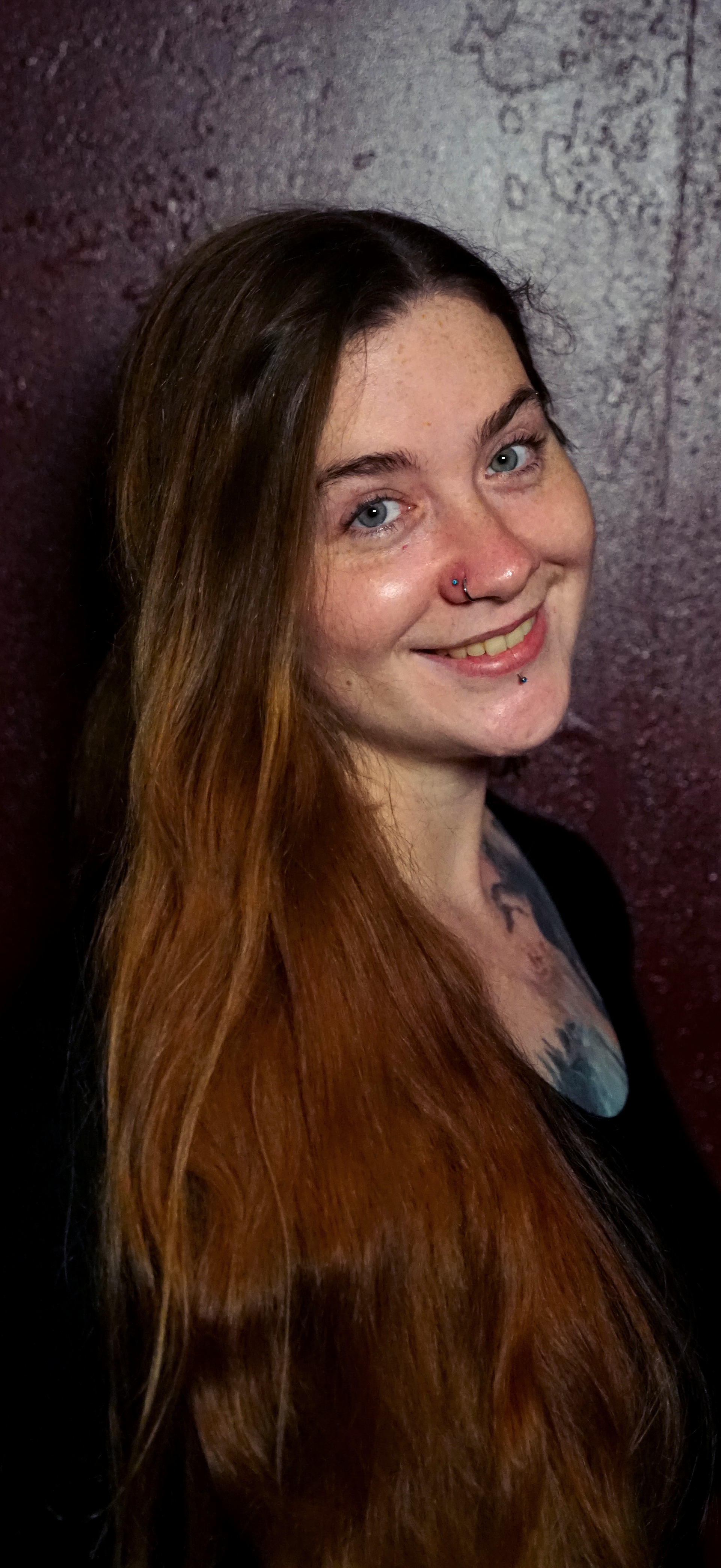 A woman with long hair and a nose ring is smiling.