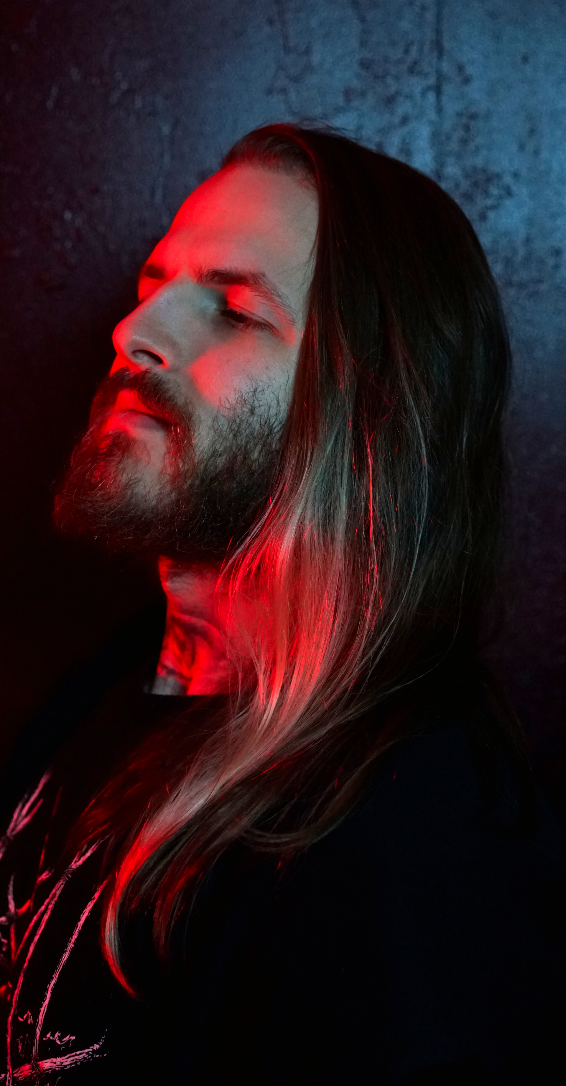 A man with long hair and a beard is standing in front of a red light.