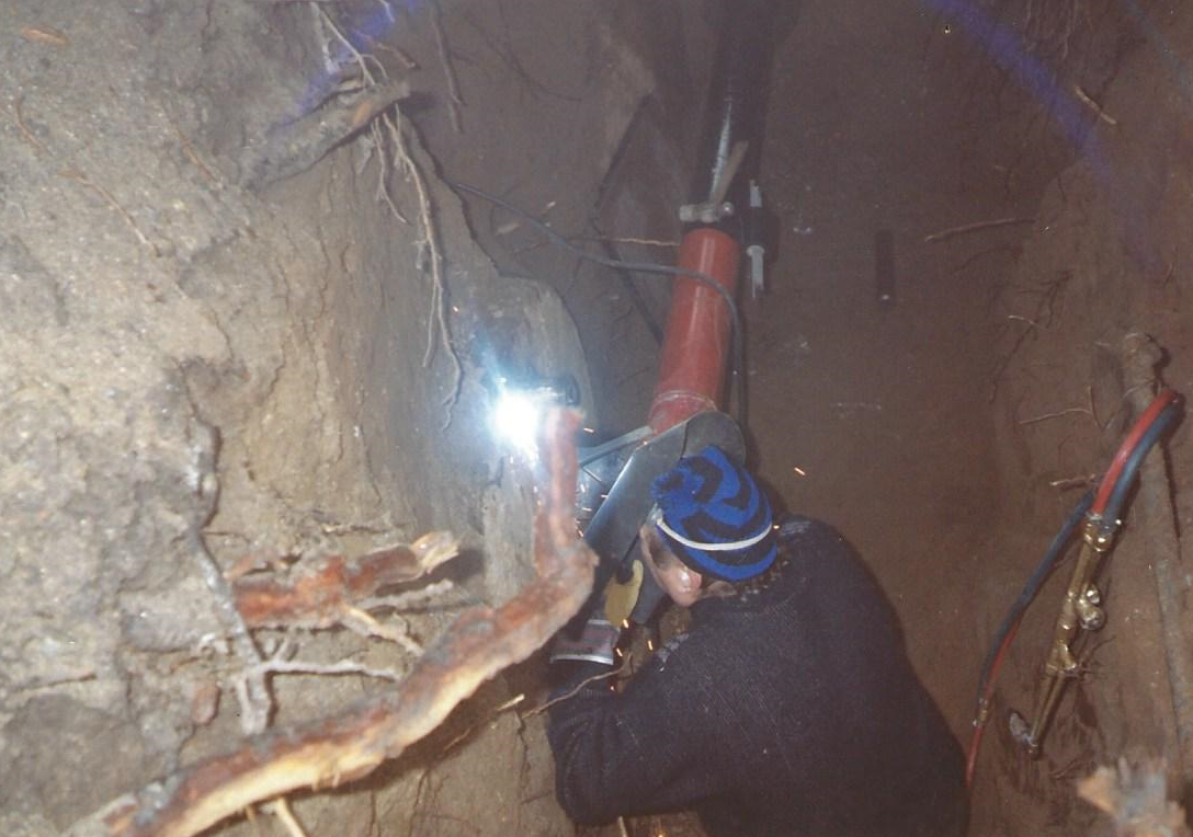 Operaio con casco blu che utilizza un attrezzo all'interno di una stretta galleria sotterranea con pareti rocciose a vista.