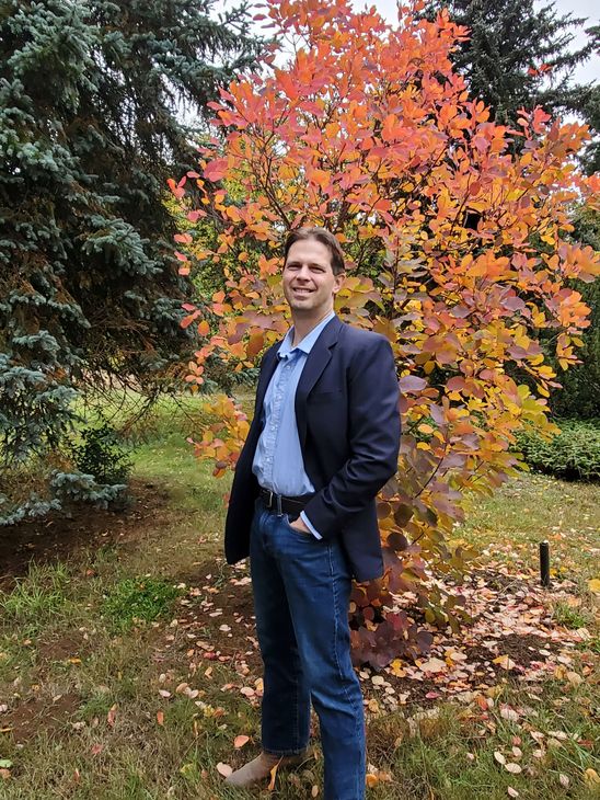 Darrel is standing outdoors in front of a small tree.