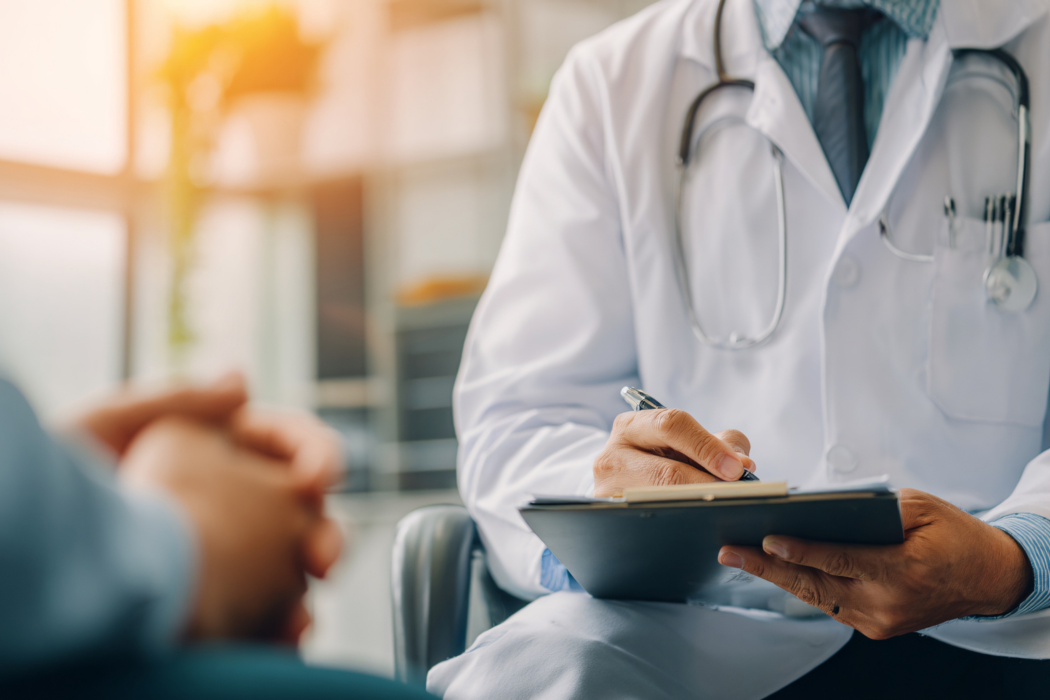 Doctor in white coat takes notes during a patient consultation indoors.