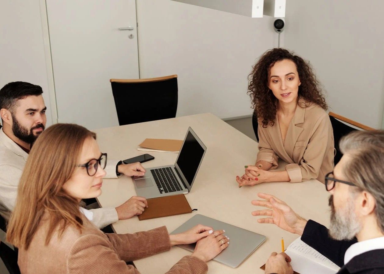 Team meeting around a conference table with laptop and notebook, discussing in a bright office