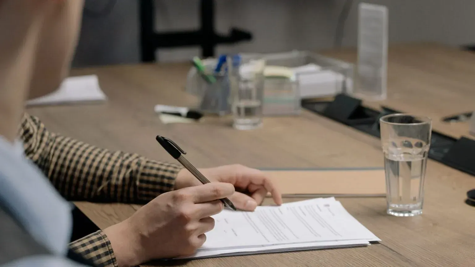 Person writing on a notepad at a meeting table with a glass of water nearby