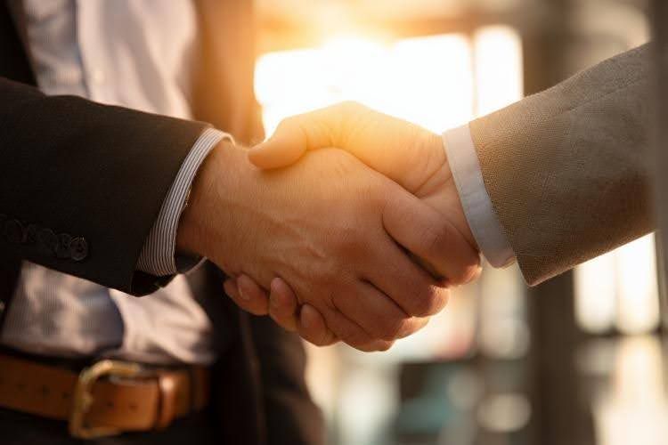 Two people in business attire shaking hands in a brightly lit office setting.