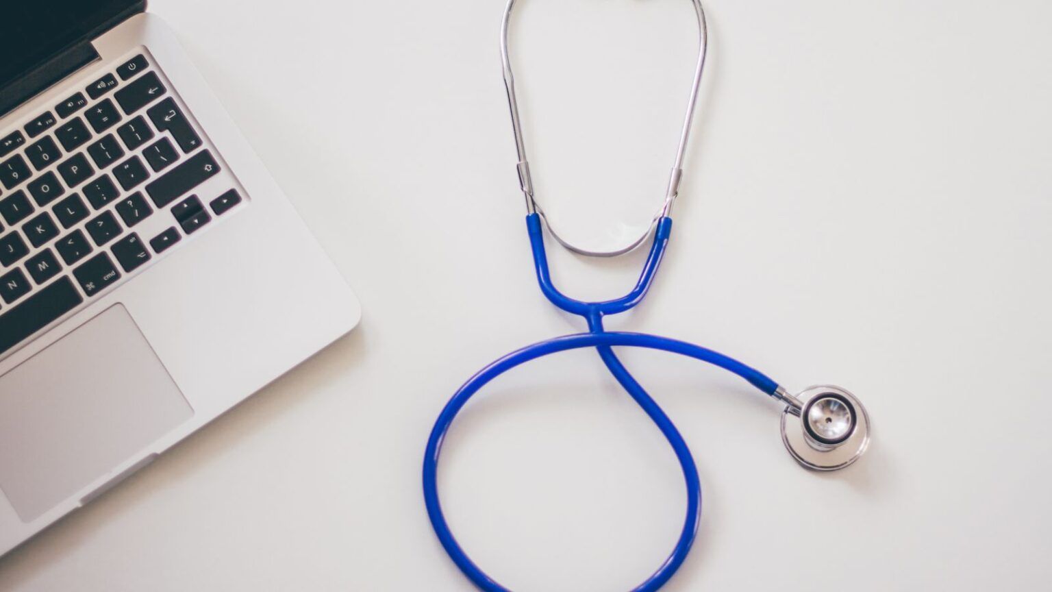 Blue stethoscope beside a laptop on a white desk