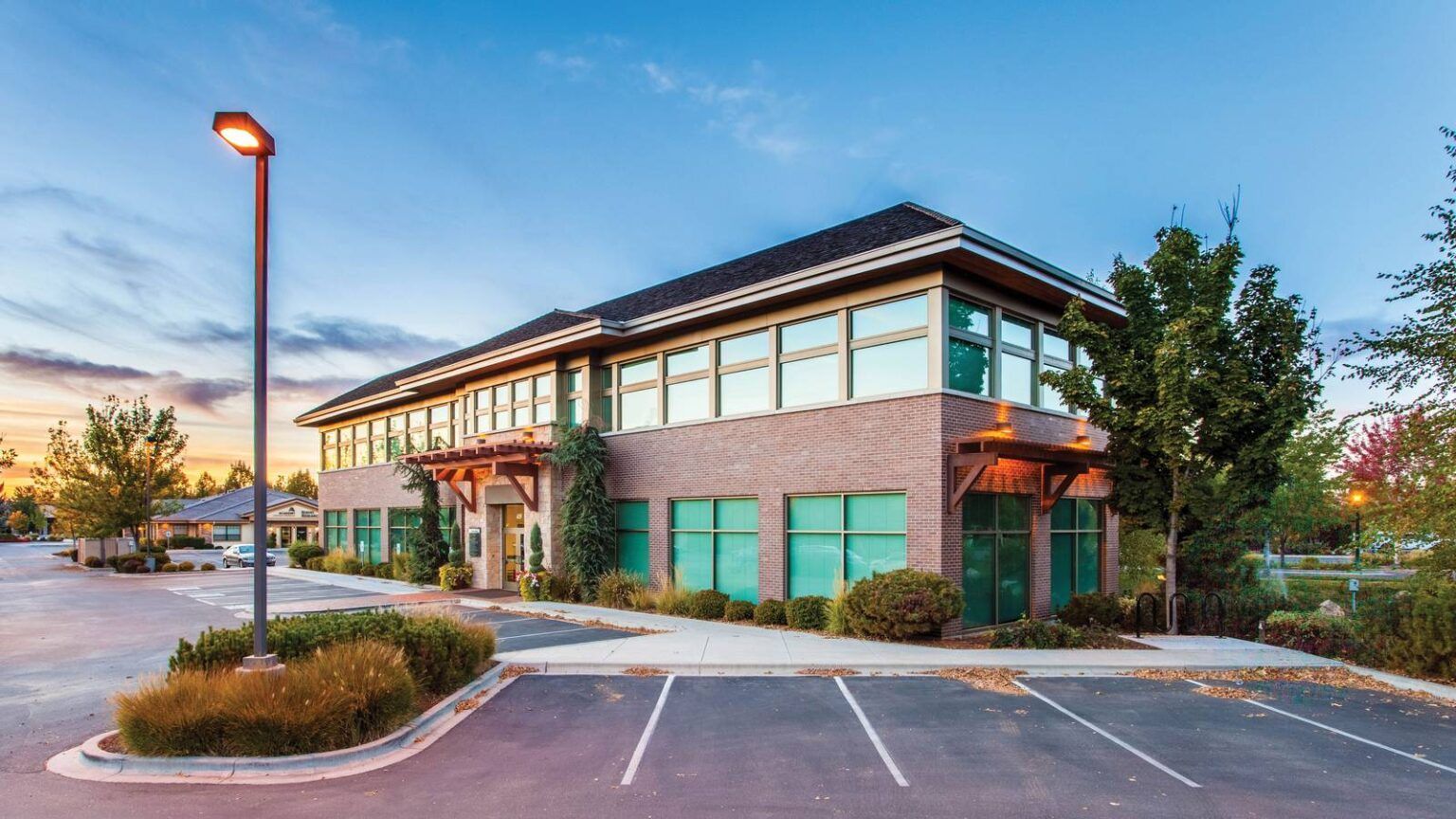 Modern two-story brick office building with teal windows and empty parking lot at dusk