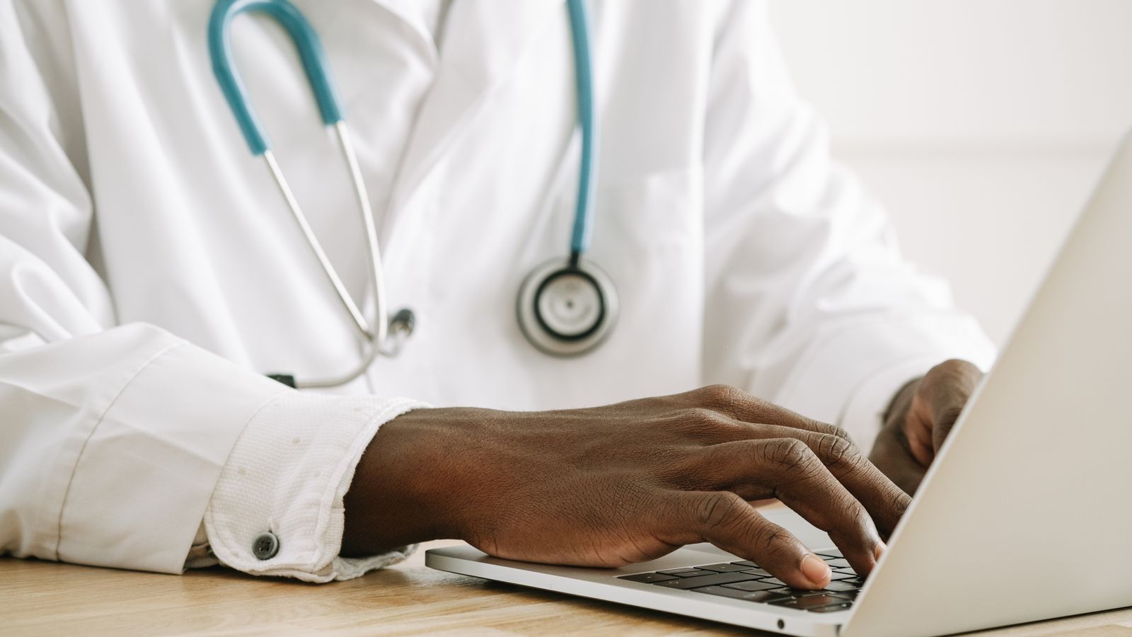 Doctor in white coat typing on a laptop with a stethoscope around the neck