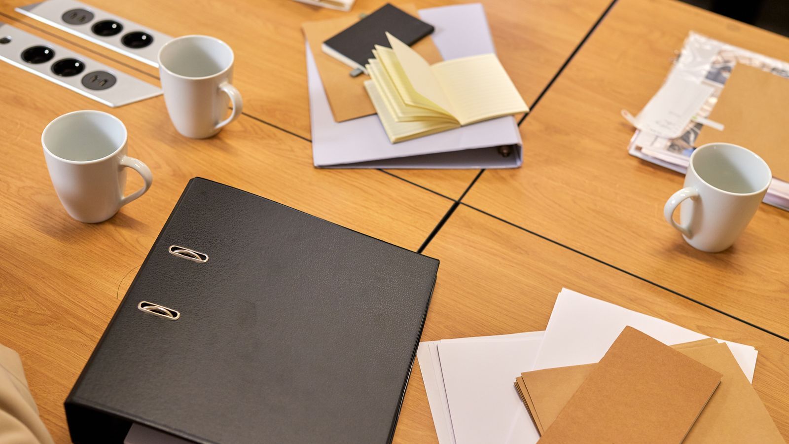 Office desk with notebooks, folders, papers, and white mugs on a wooden table.