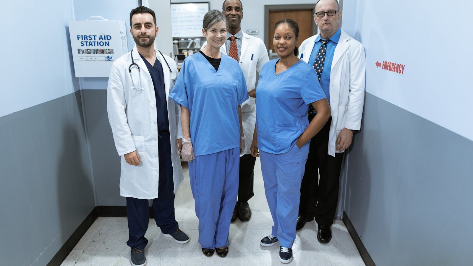 Four medical staff in scrubs and lab coats standing in a hospital hallway
