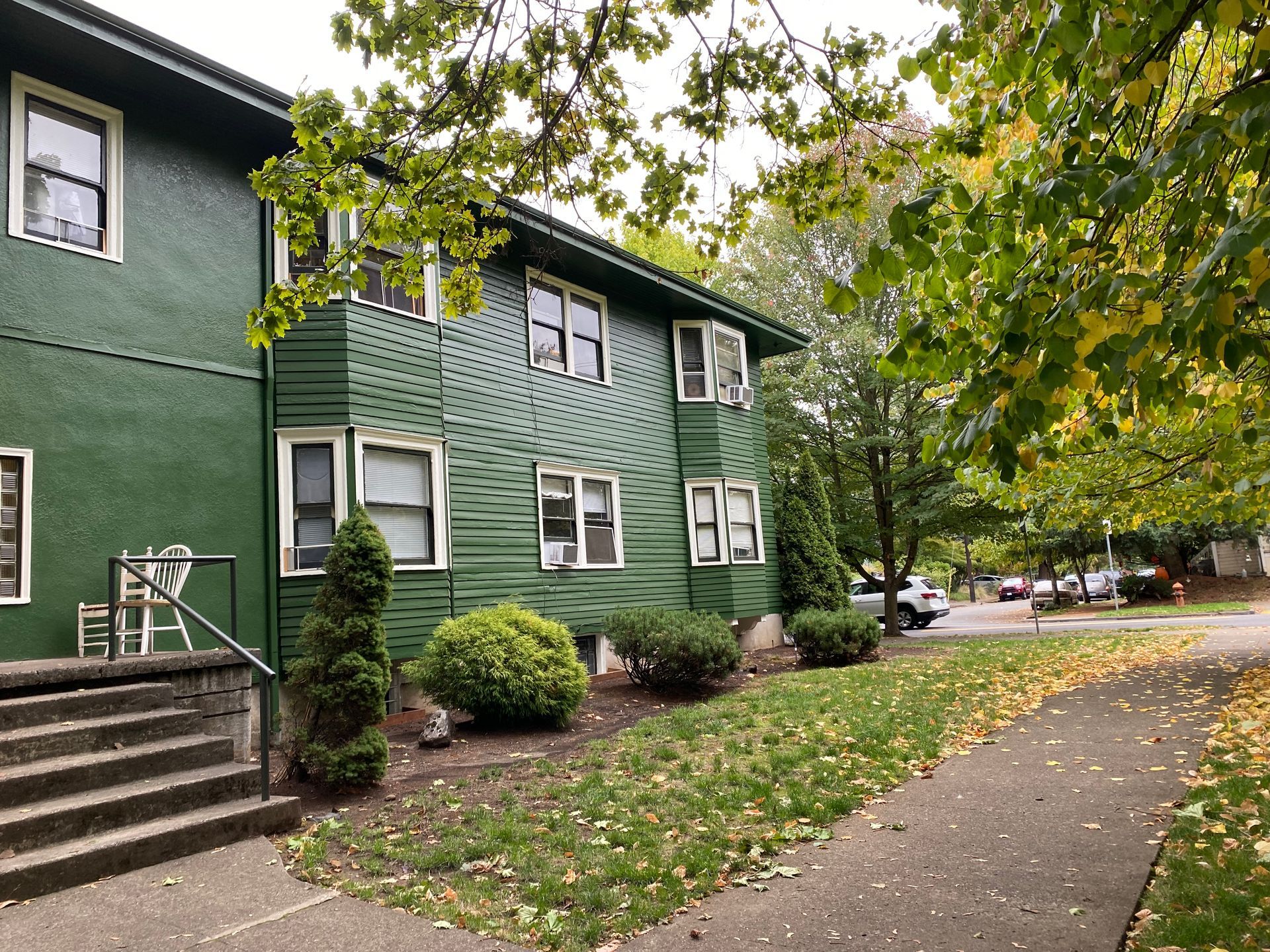 Green apartment building beside a tree-lined sidewalk with steps and fallen leaves