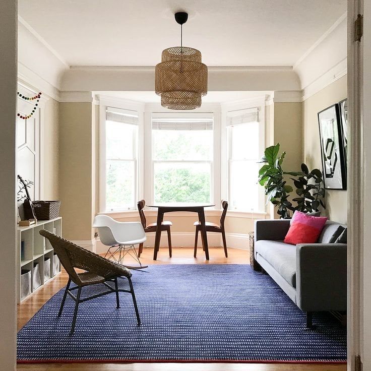 Bright living room with bay window, blue rug, gray sofa, wicker chair, and indoor plants