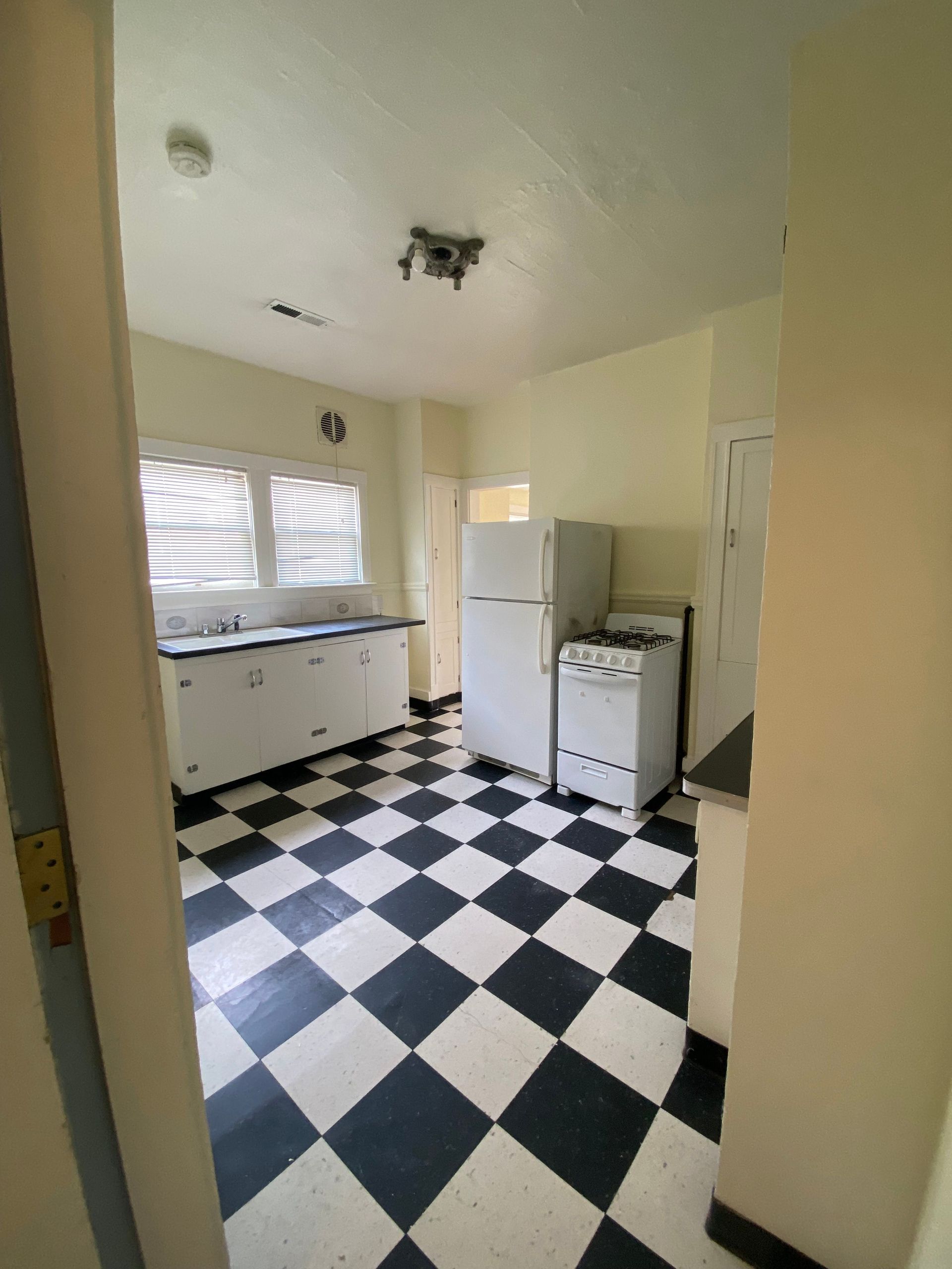 Small kitchen with black-and-white checkered floor, white cabinets, fridge, and stove.
