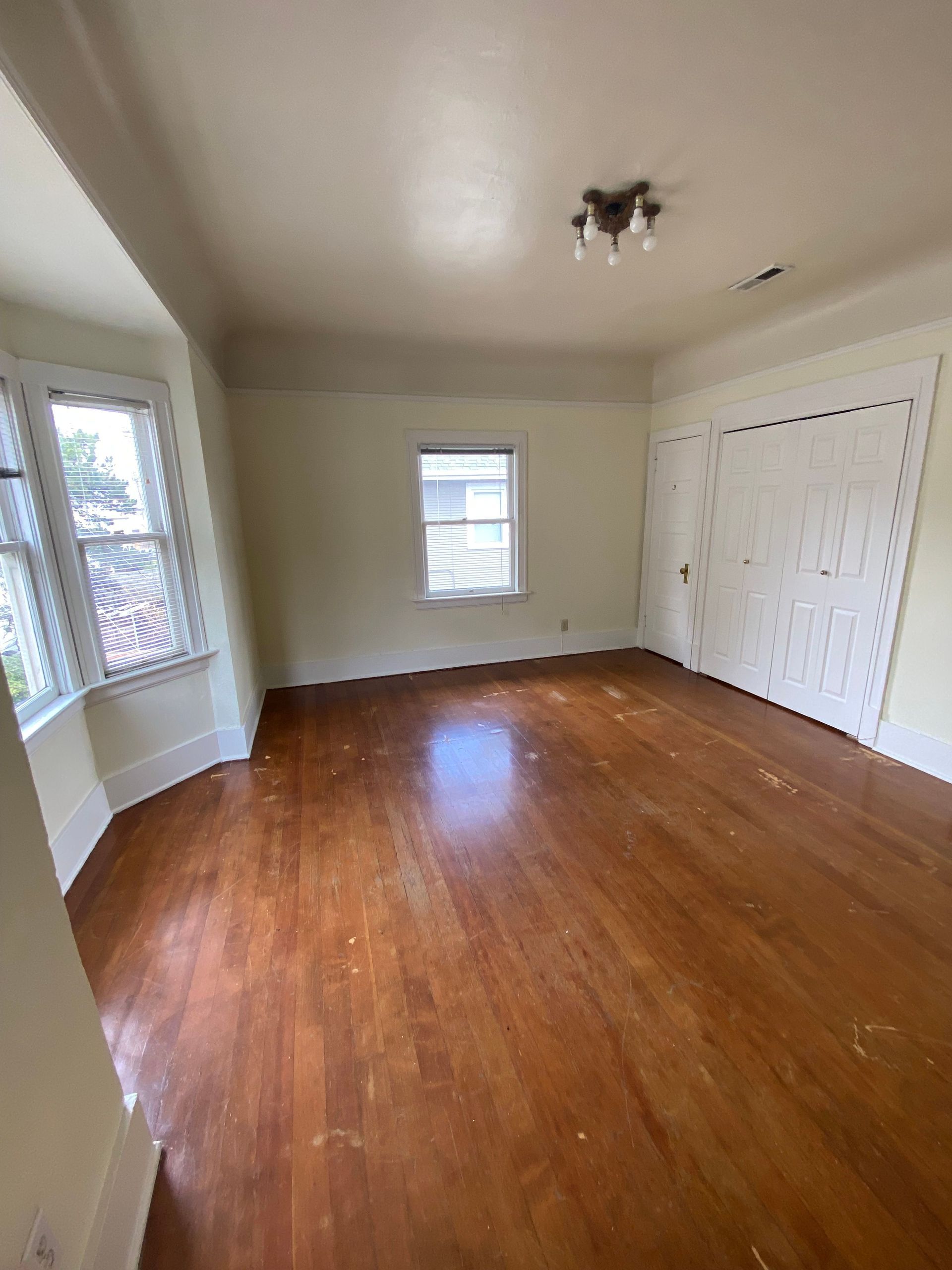 Empty room with hardwood floors, white walls, windows, and closet doors.