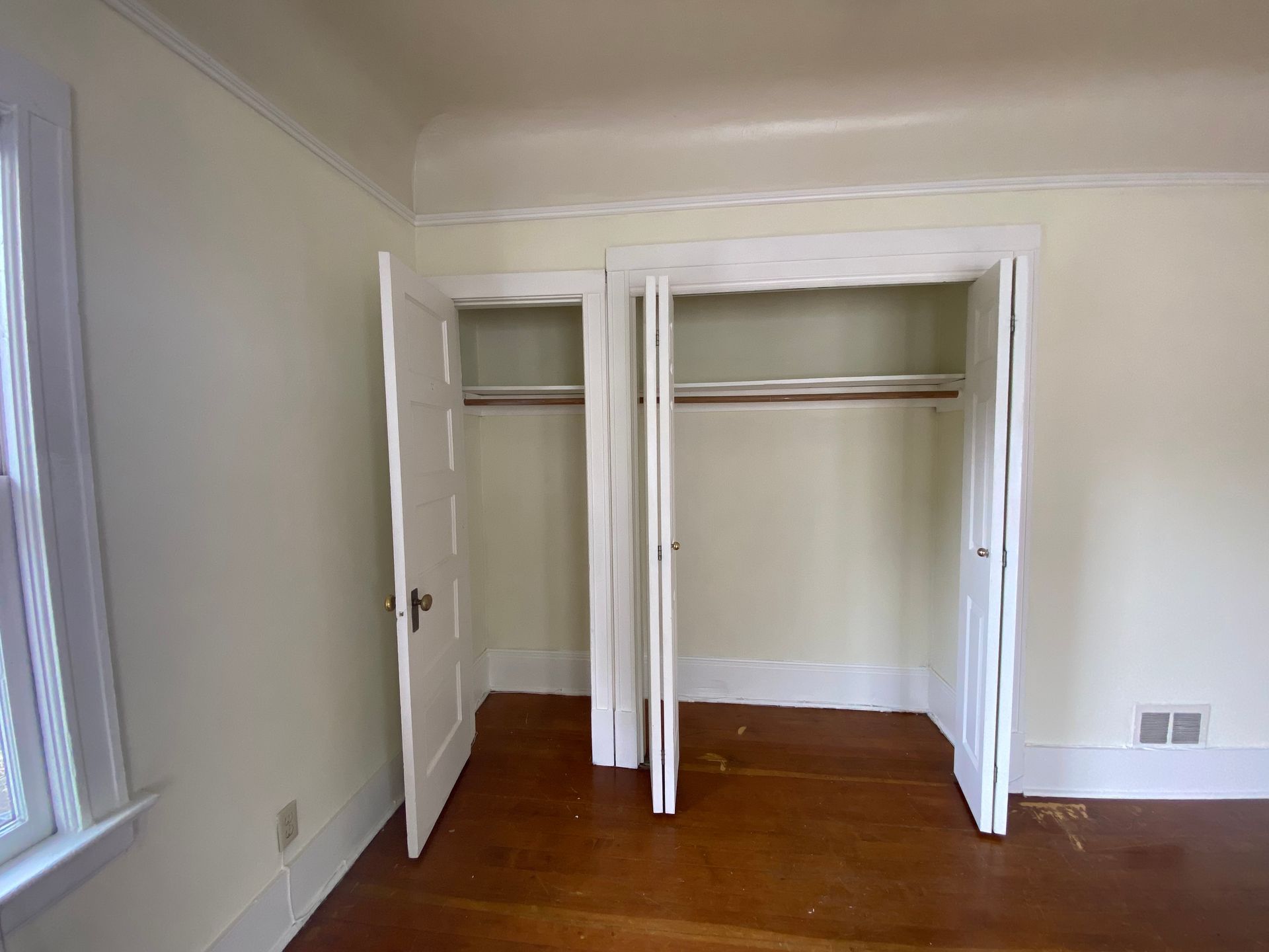 Empty bedroom closet with open white doors, wood floor, and window light