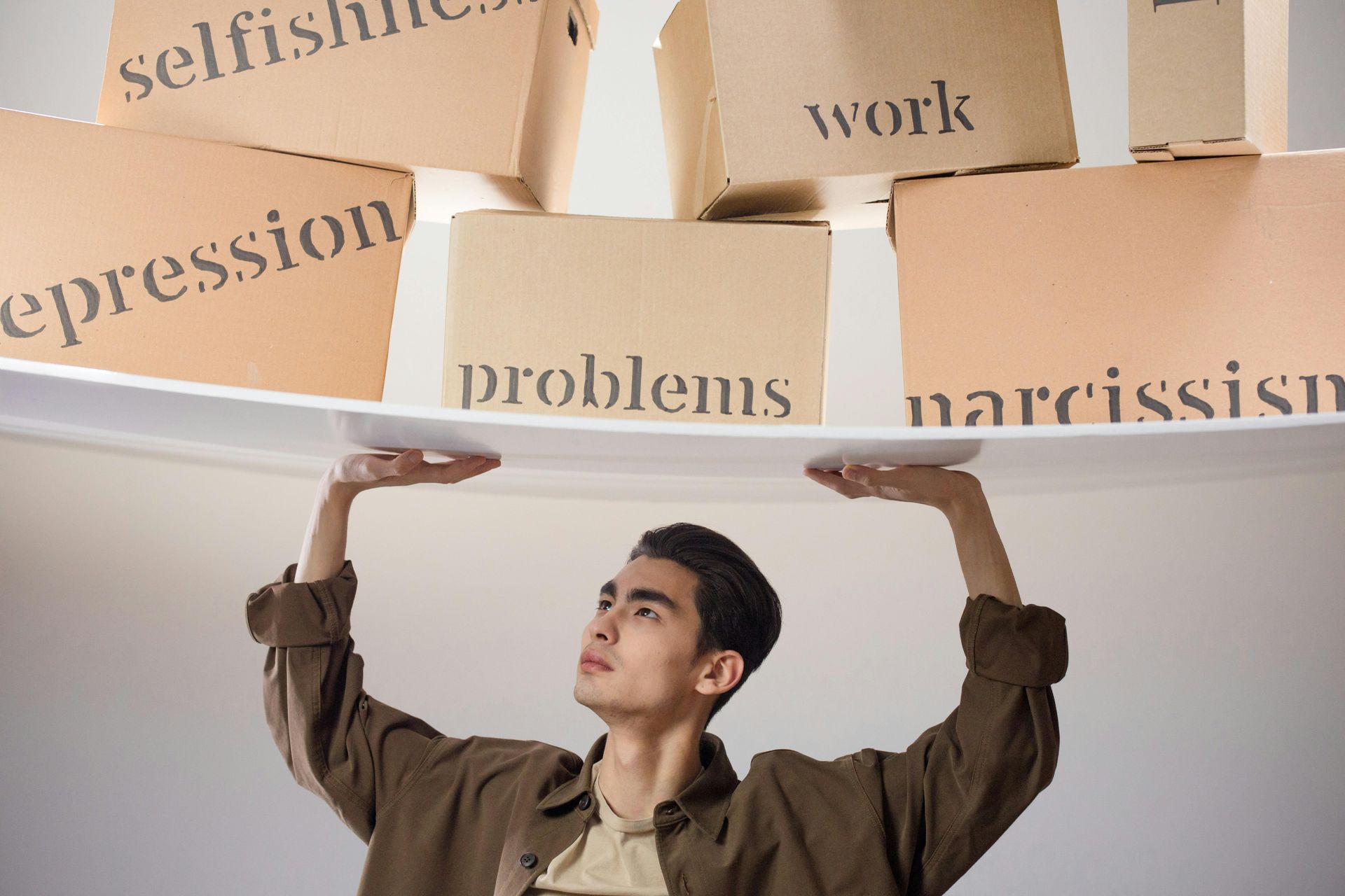 A person holds up a board balancing heavy cardboard boxes labeled with words like