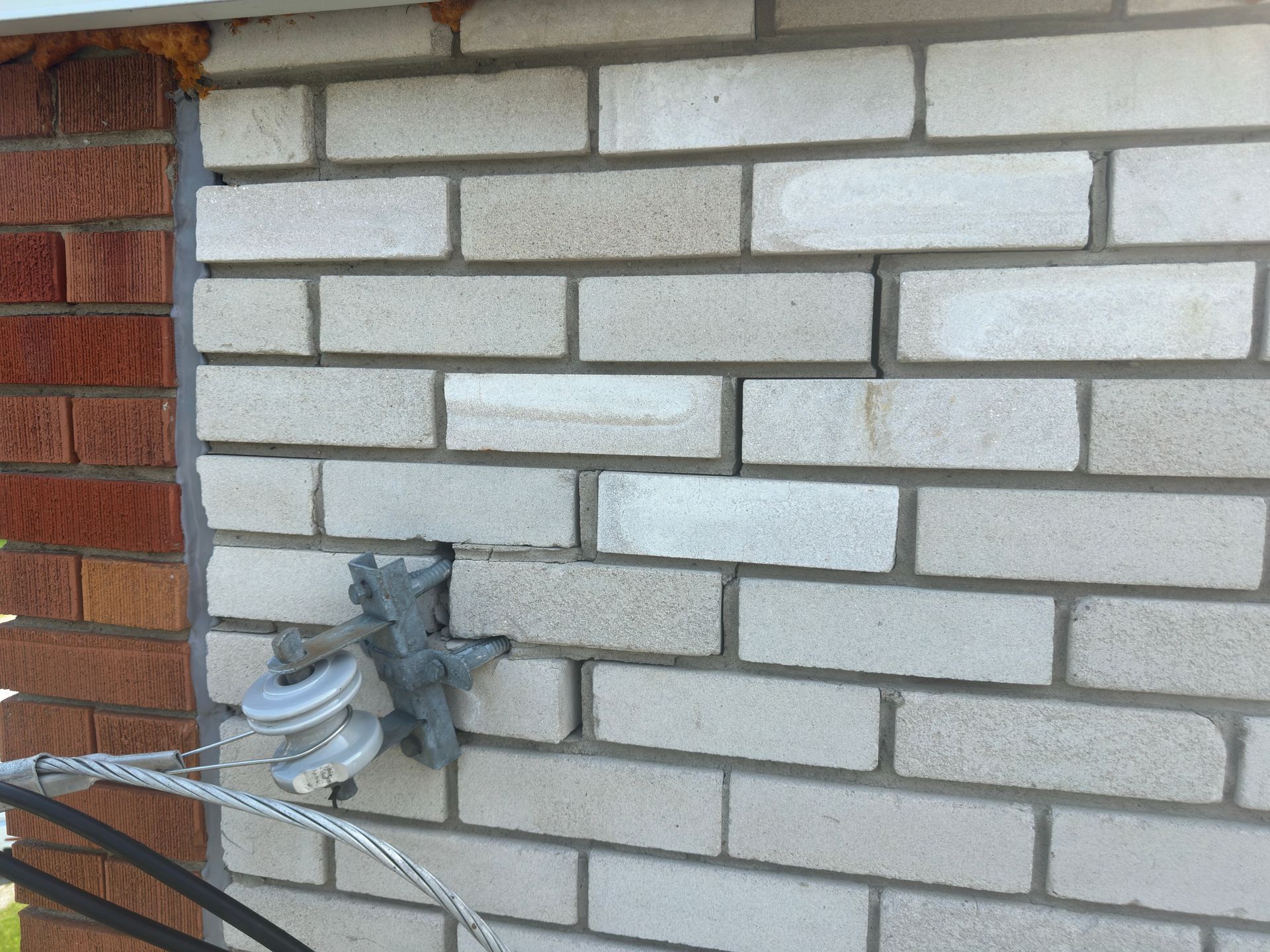 Mur de briques blanchâtres avec une fissure, un appareil électrique et une section de mur en briques rouge-brun.