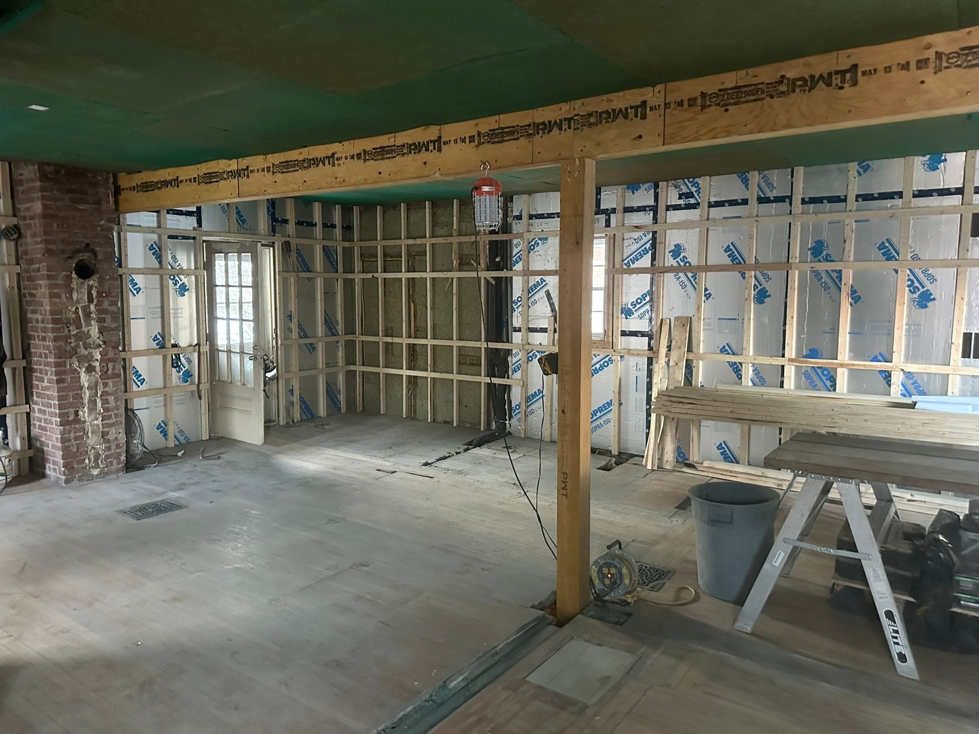 Pièce en rénovation avec montants muraux apparents, isolation et briques partiellement démolies.