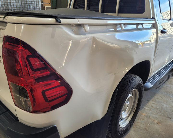 A white truck with a damaged bumper is parked in a garage.