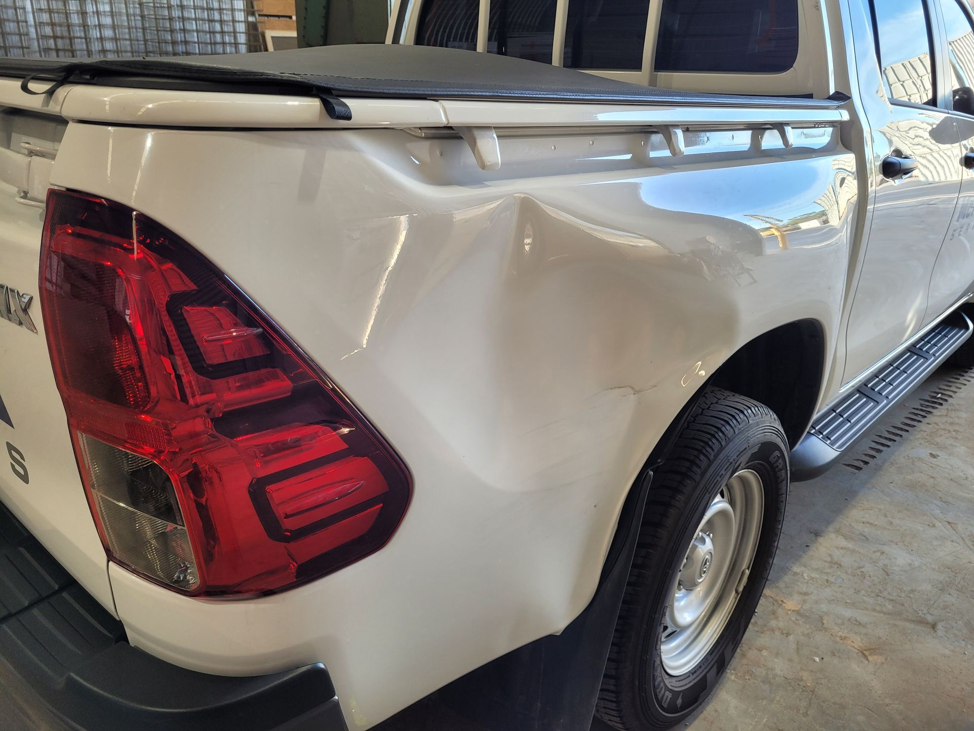 A white truck with a damaged fender is parked in a garage.