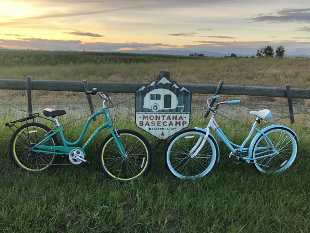 Two teal bicycles beside a fence at sunset with a farmhouse sign in the background