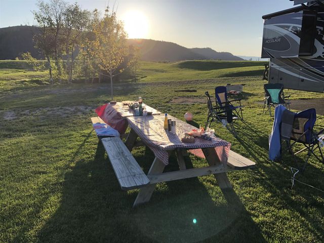 Sunlit picnic table on grassy field beside an RV, with mountains in the background.