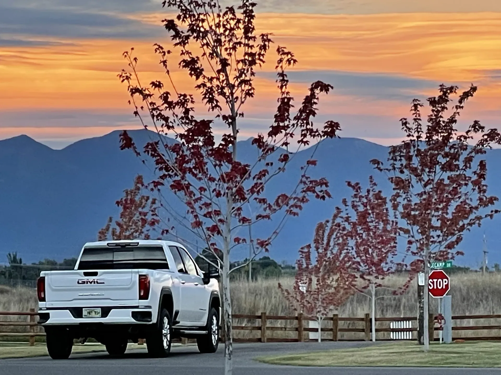 White pickup truck near a stop sign at sunset, with mountains in the background.