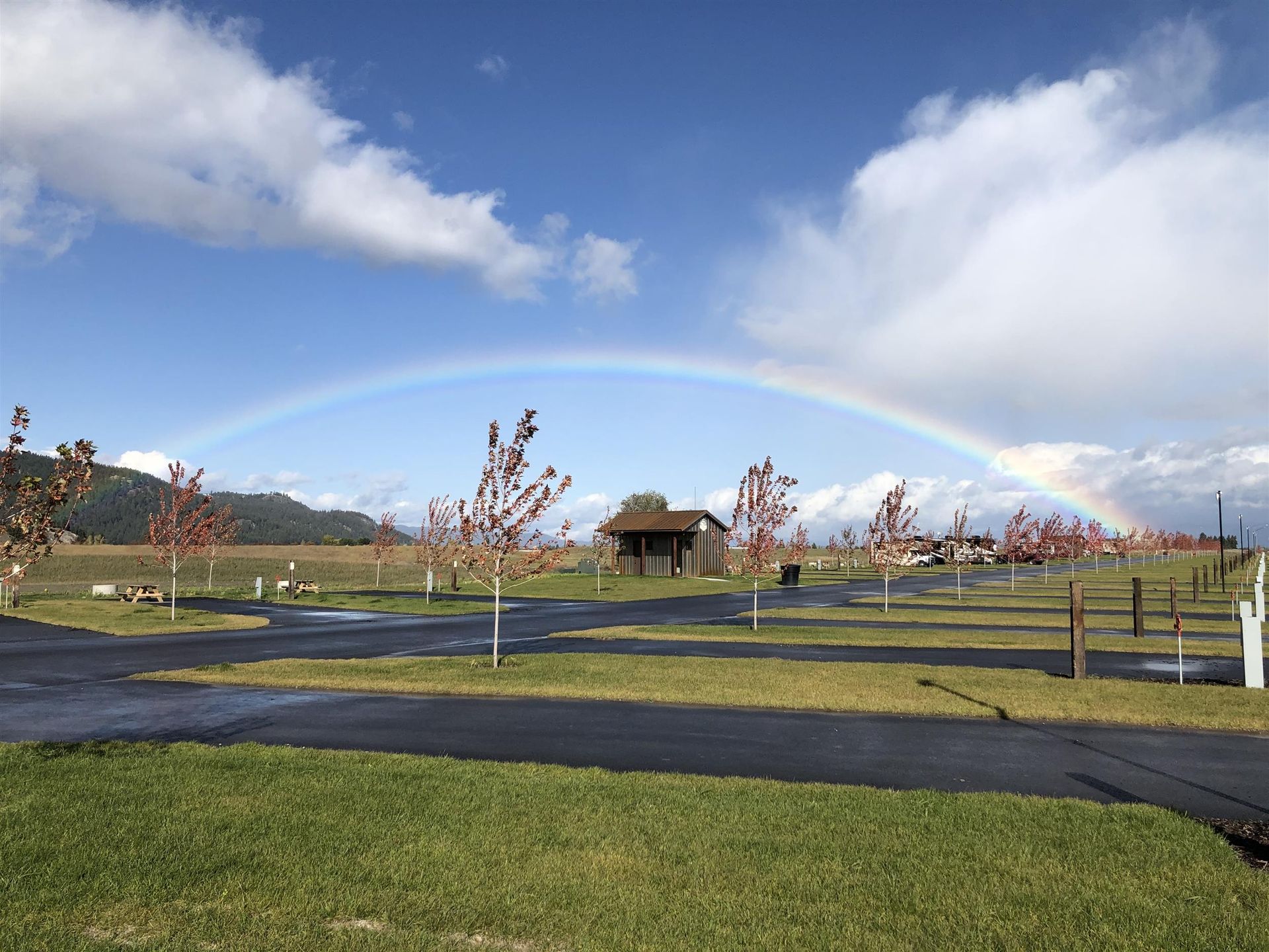 Rainbow over a grassy park with a small shelter and cloudy sky