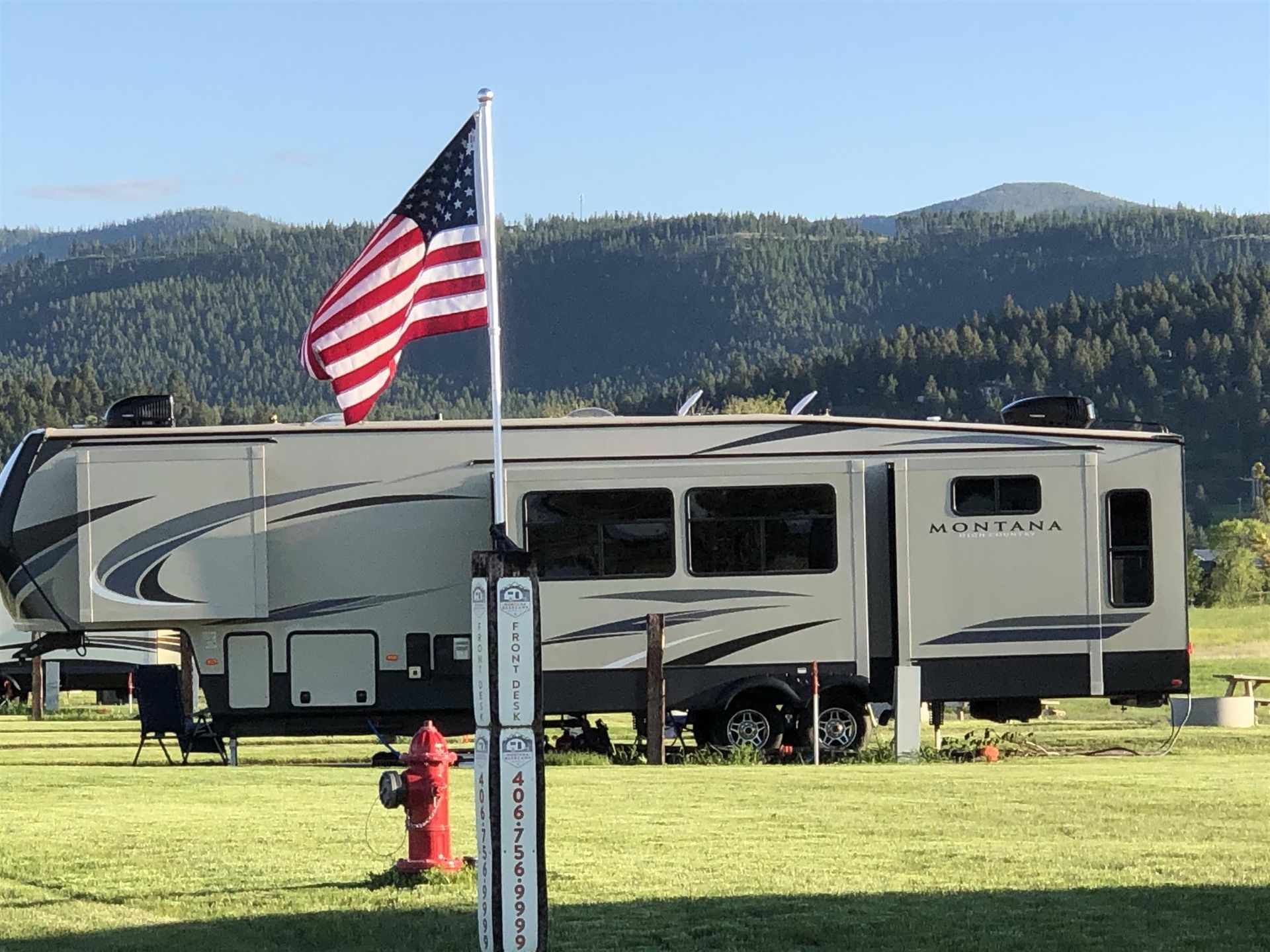 Large RV parked on grass with an American flag and mountains in the background