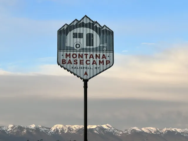 Montana Basecamp sign on a pole against snowy mountains and a cloudy sky